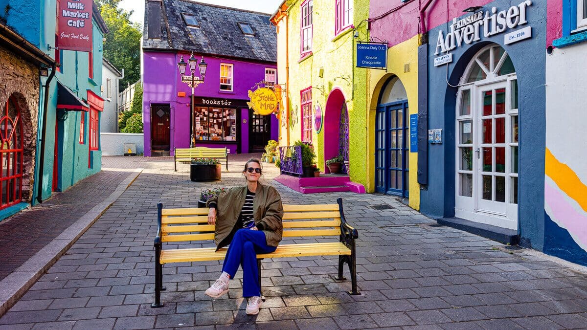 Frau auf Bank umgeben von bunten Häuserfassaden in Kinsale Irland