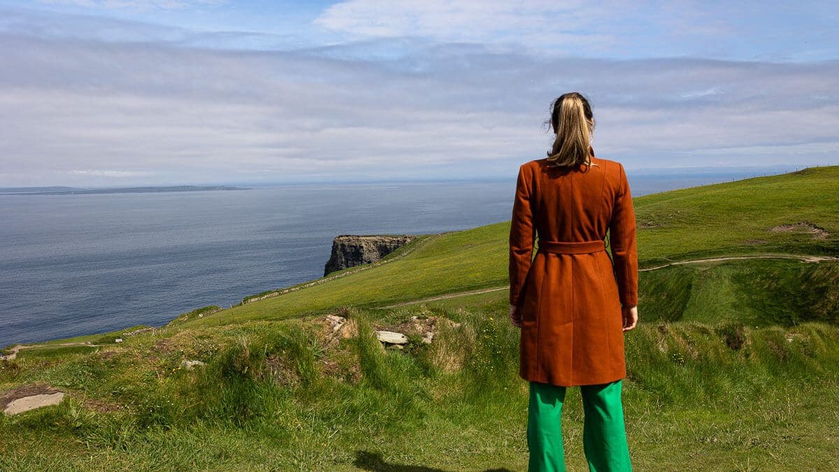 Frau in rostrotem Mantel schaut auf Cliffs of Moher