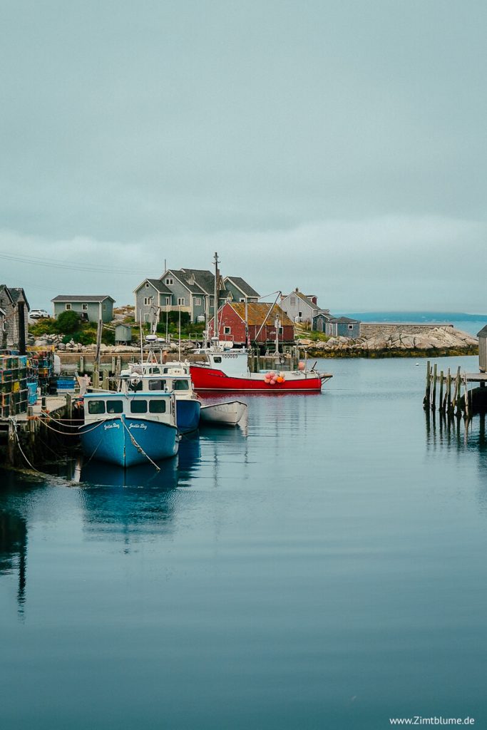 Blick auf die idyllische Hafenbucht von Peggy’s Cove mit Fischerbooten und Stegen.