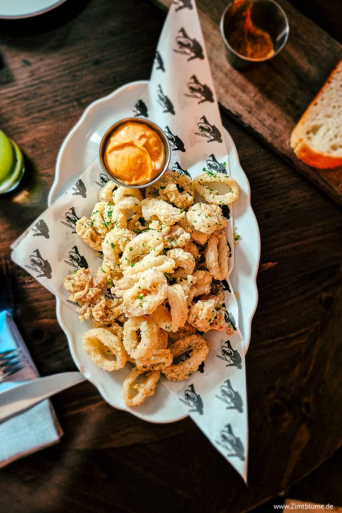 Goldbraun ausgebackene Calamari-Ringe an einer cremigen Dip-Sauce aus getrockneten Tomaten, serviert auf einem weißen Teller im The Bicycle Thief.